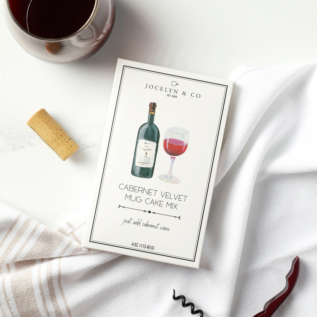 Jocelyn & Co. Cabernet Velvet Mug Cake Mix package with a glass of red wine, cork, and corkscrew on a white surface.