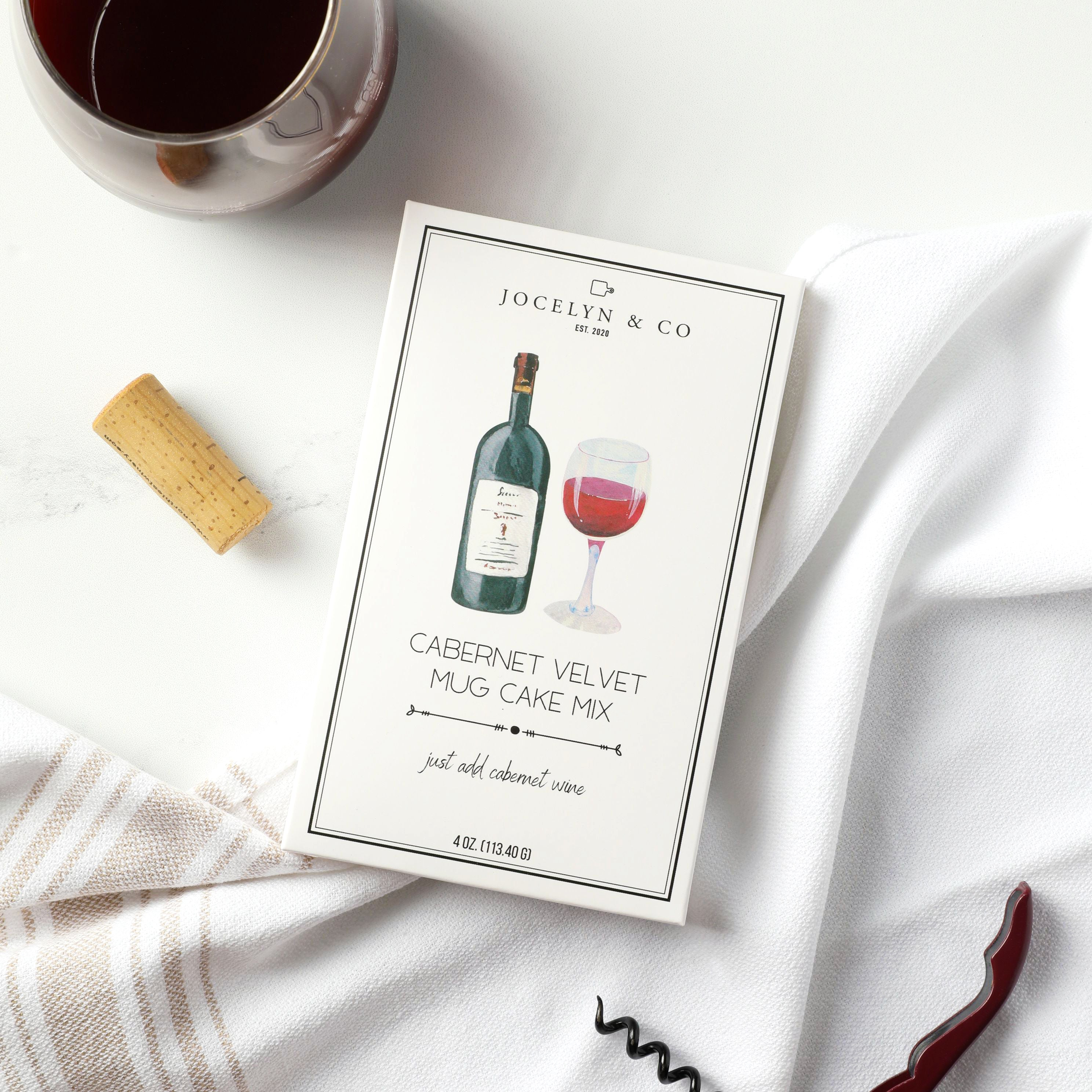 Jocelyn & Co. Cabernet Velvet Mug Cake Mix package with a glass of red wine, cork, and corkscrew on a white surface.