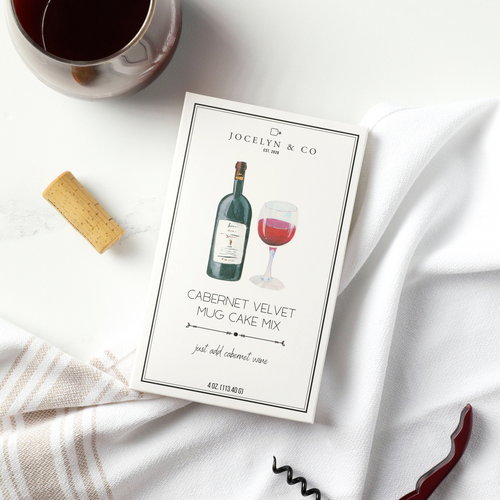 Jocelyn & Co. Cabernet Velvet Mug Cake Mix package with a glass of red wine, cork, and corkscrew on a white surface.