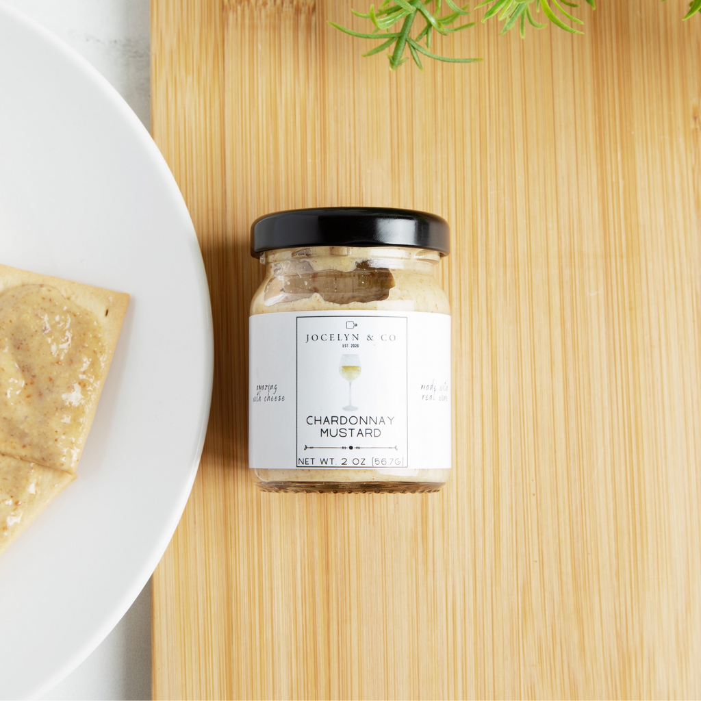 Jar of chardonnay jelly on a wooden board with crackers and a white plate.