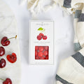 Box of organic fruit snacks with cherries on a marble surface and striped towel.