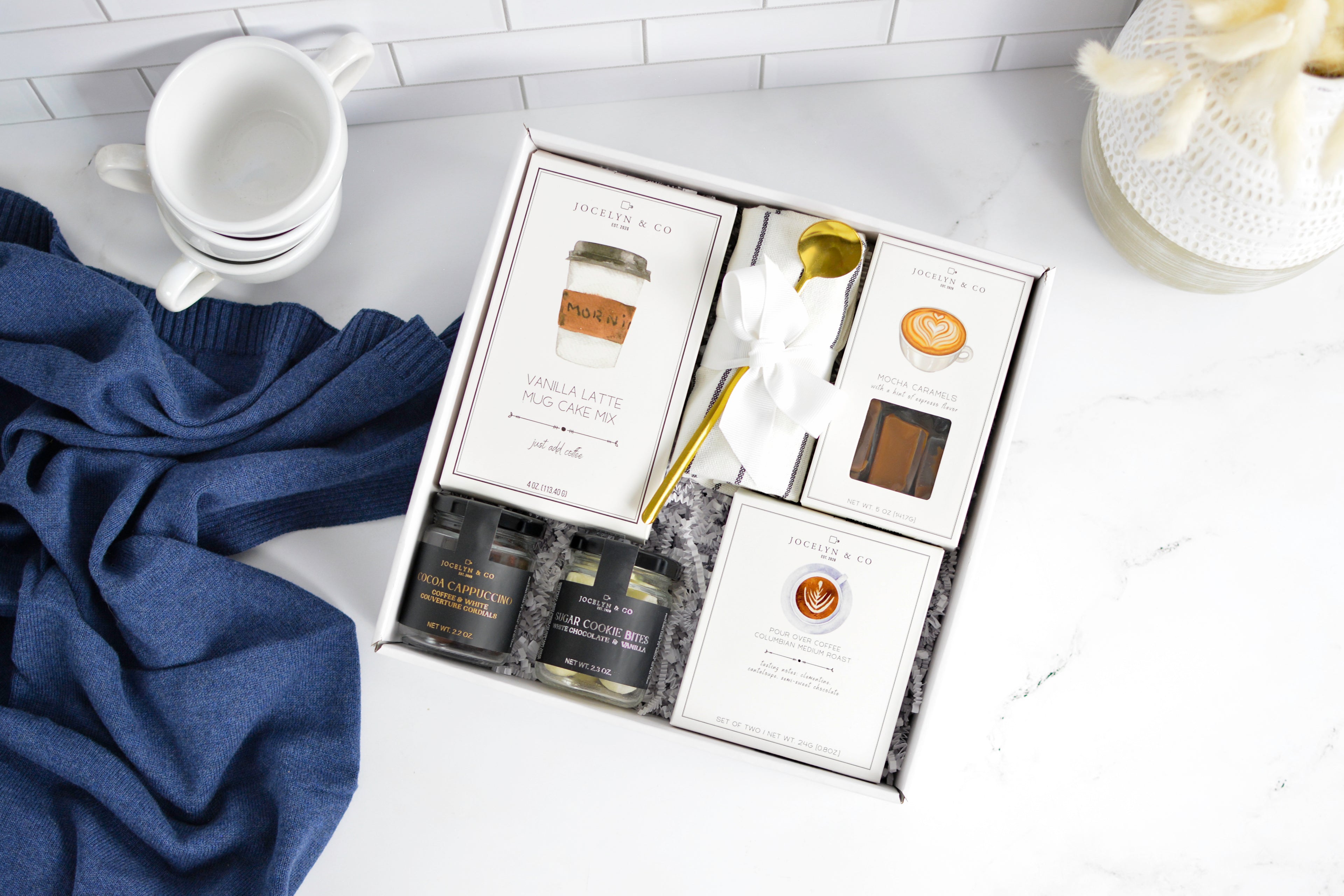 Coffee gift set with packaging on a white surface with a blue towel and white teacups.