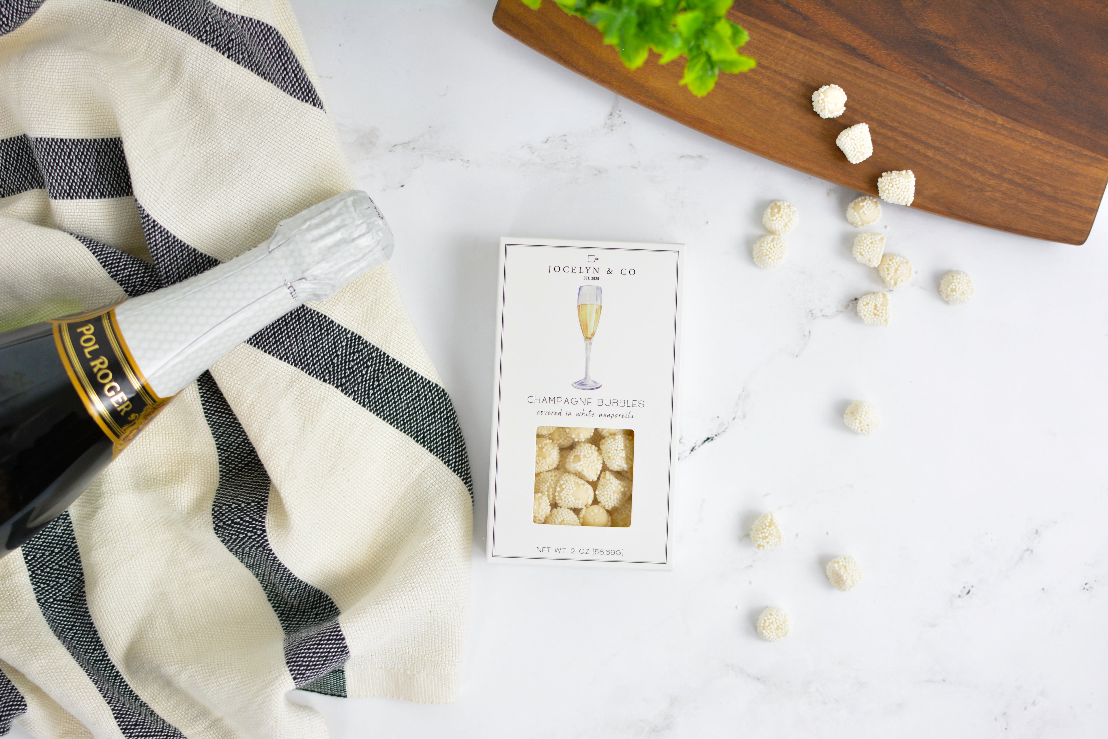 Bottle of champagne, decorative box, and decorative items on a white surface with a black and white striped towel.