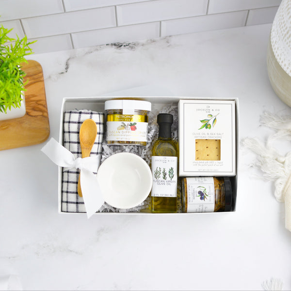 Gift set with kitchen items including a bowl, bottles, and jars on a marble countertop.