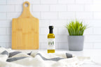 Bottle of olive oil on a kitchen counter with a cutting board and plant in the background.
