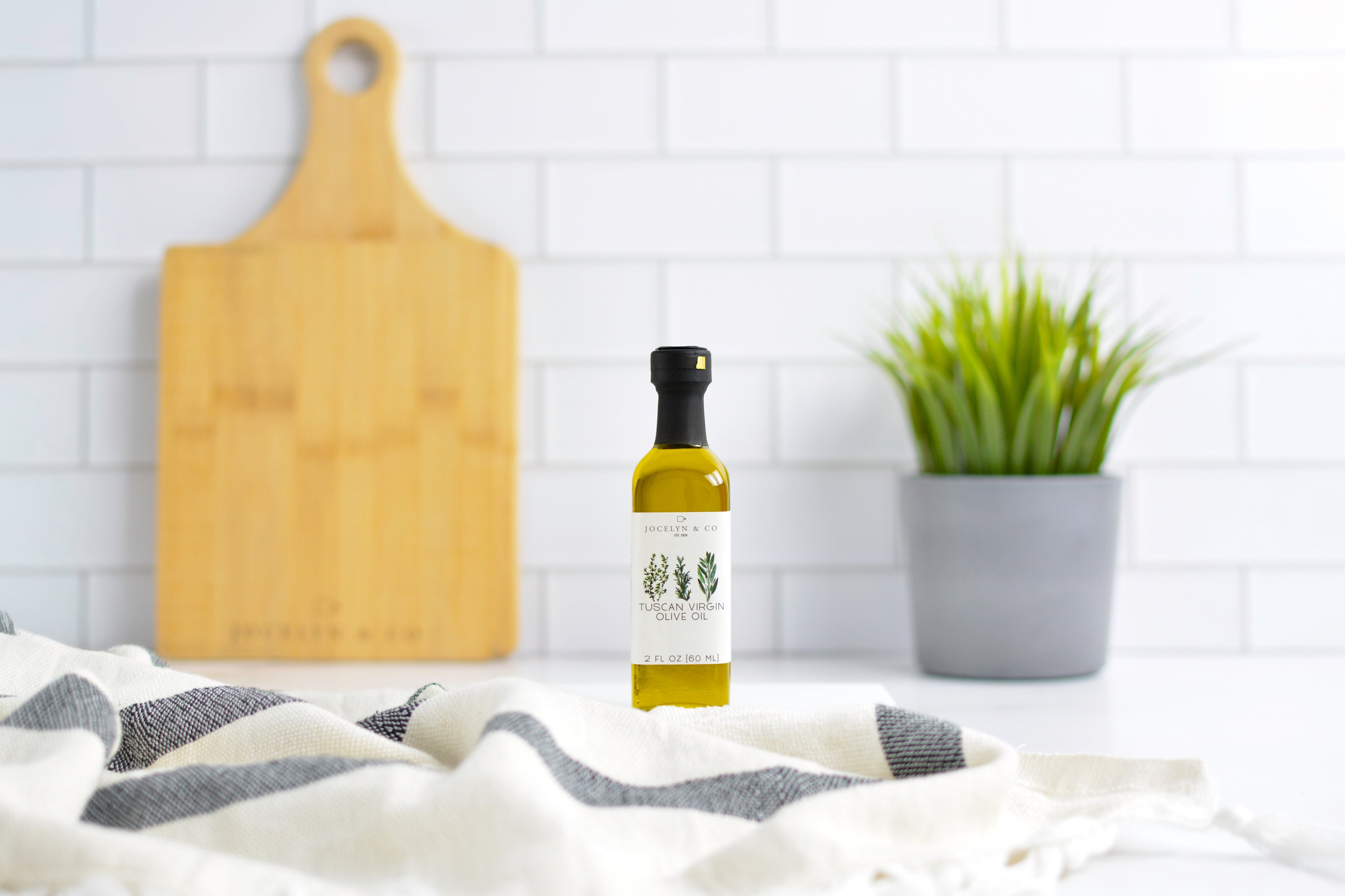 Bottle of olive oil on a kitchen counter with a cutting board and plant in the background.