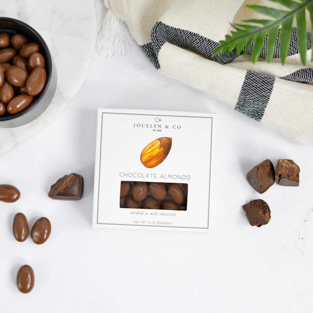 Chocolate almonds with a box on a marble surface with a striped cloth and plant in the background