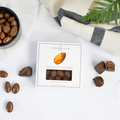 Chocolate almonds with a box on a marble surface with a striped cloth and plant in the background